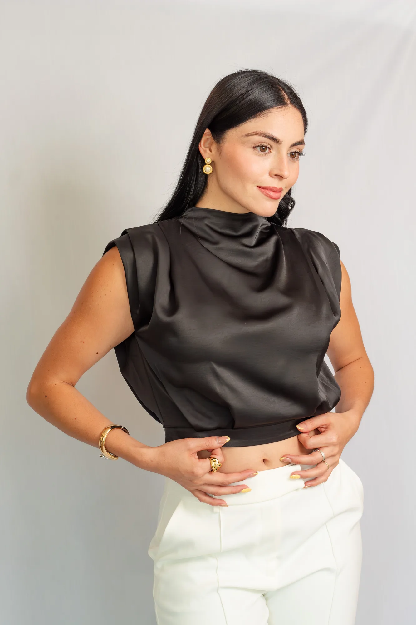 Modelo con blusa corta de satín negro y cuello drapeado, con pantalón blanco.